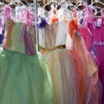 An array of colorful little girl's party or princess dresses for sale at outdoor vendor