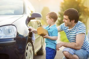 Young father with his little son washing car