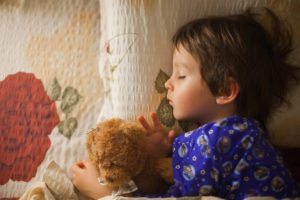 Adorable little boy sleeping at night with his teddy bear friend